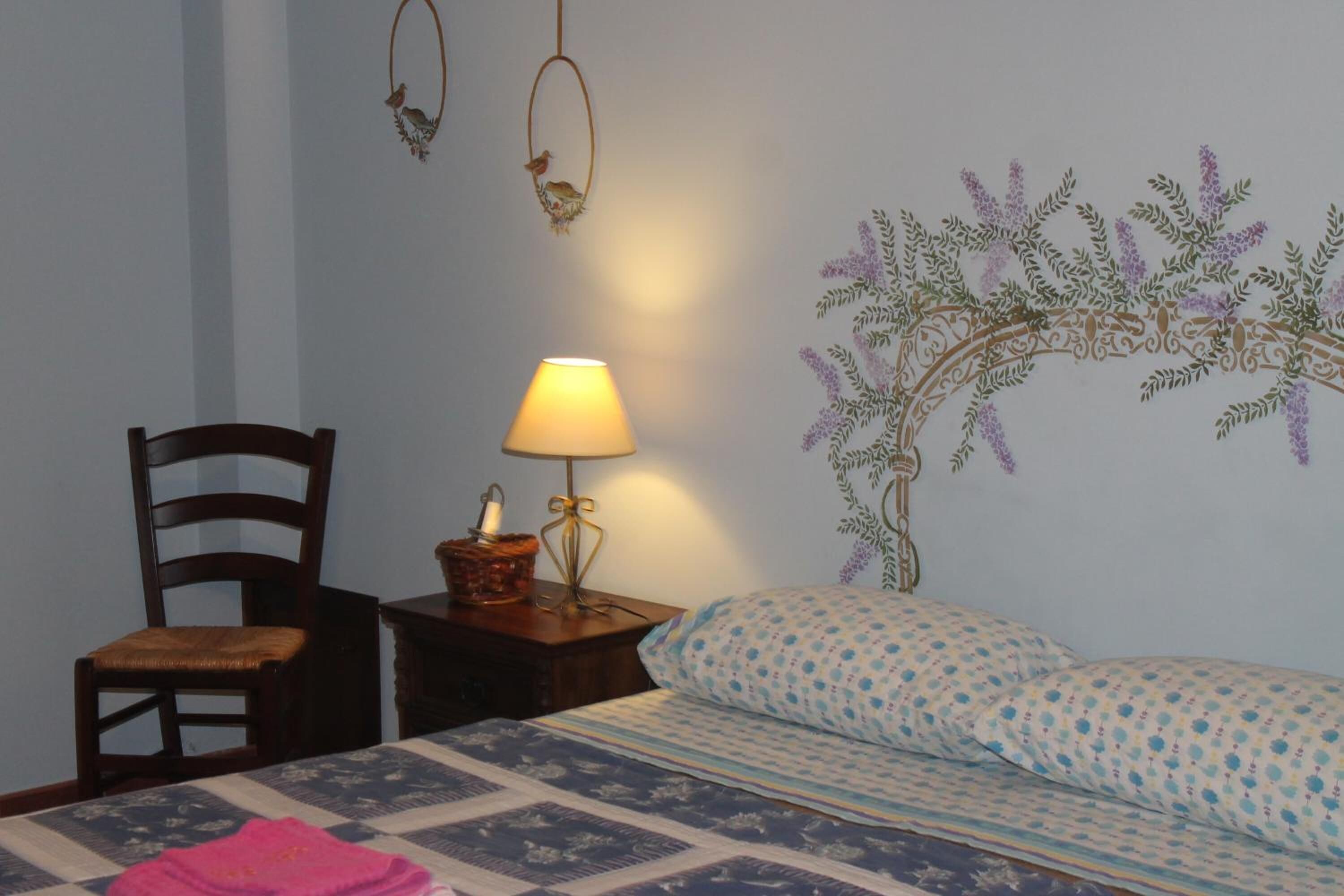 Ein Schlafzimmer mit Bett, Stuhl, Nachttisch mit Lampe und Wanddekoration.