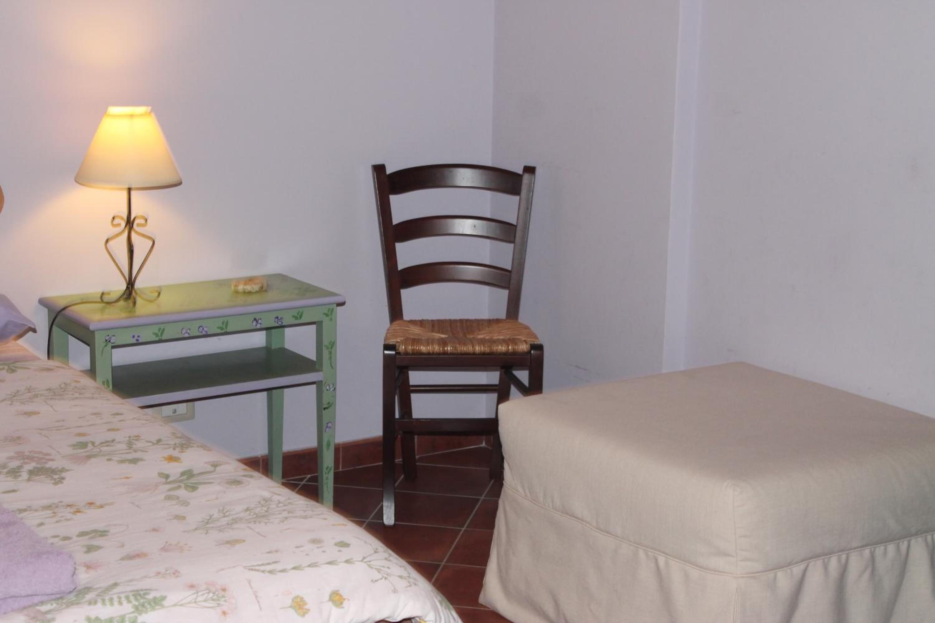 Ein kleines Zimmer mit einem Bett, einem Sessel, einem Tisch und einer Lampe.