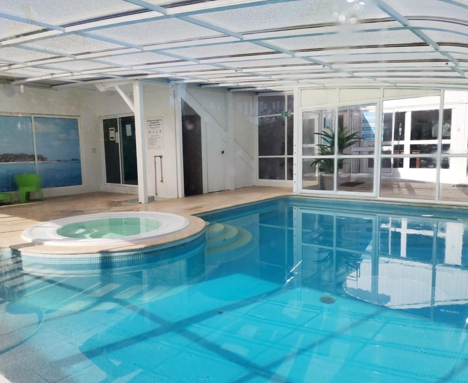 Piscina interior con jacuzzi, puertas de cristal y vistas al exterior.