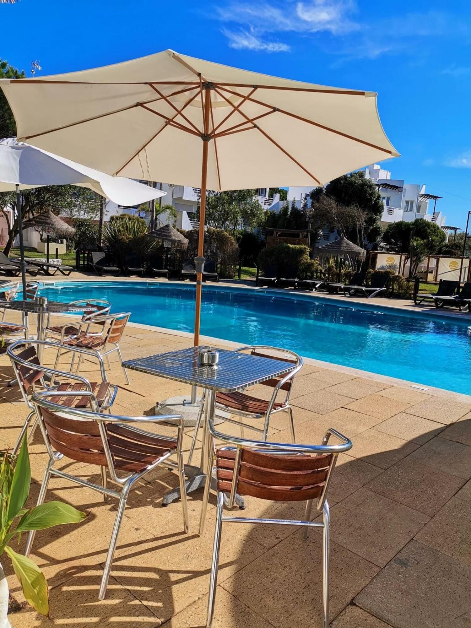 A poolside area with lounge chairs, a table, and umbrellas.