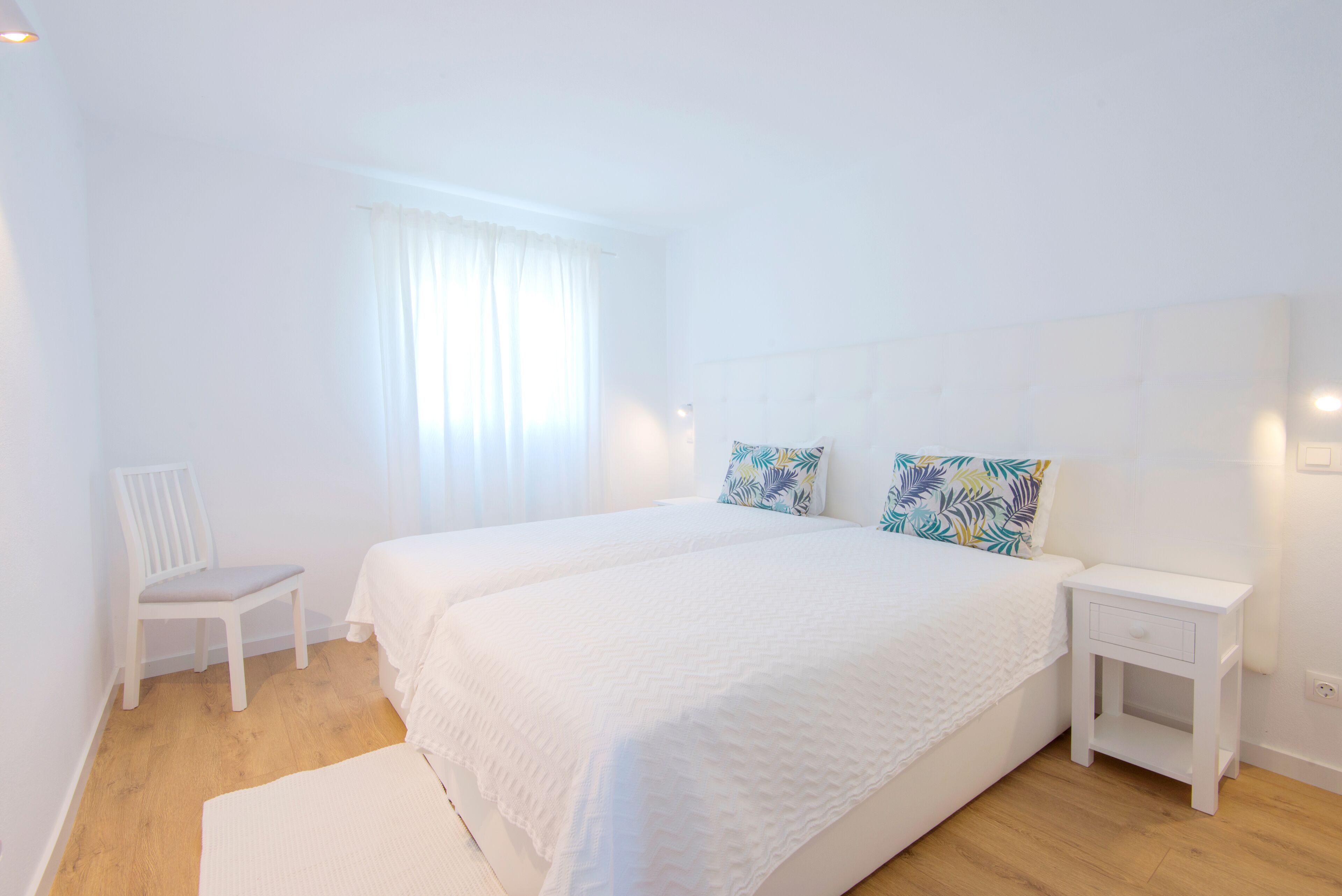 A bedroom with a large bed, a chair, a bedside table, and a window with curtains.