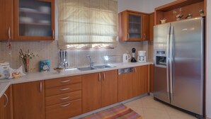 Una cocina con gabinetes de madera, un refrigerador de acero inoxidable, un lavamanos y una ventana con cortina.