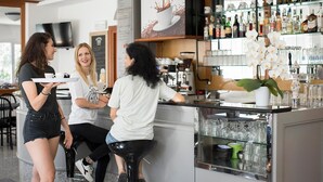 Uma área de bar com uma máquina de café, prateleiras com garrafas e uma vitrine de vidro com copos.