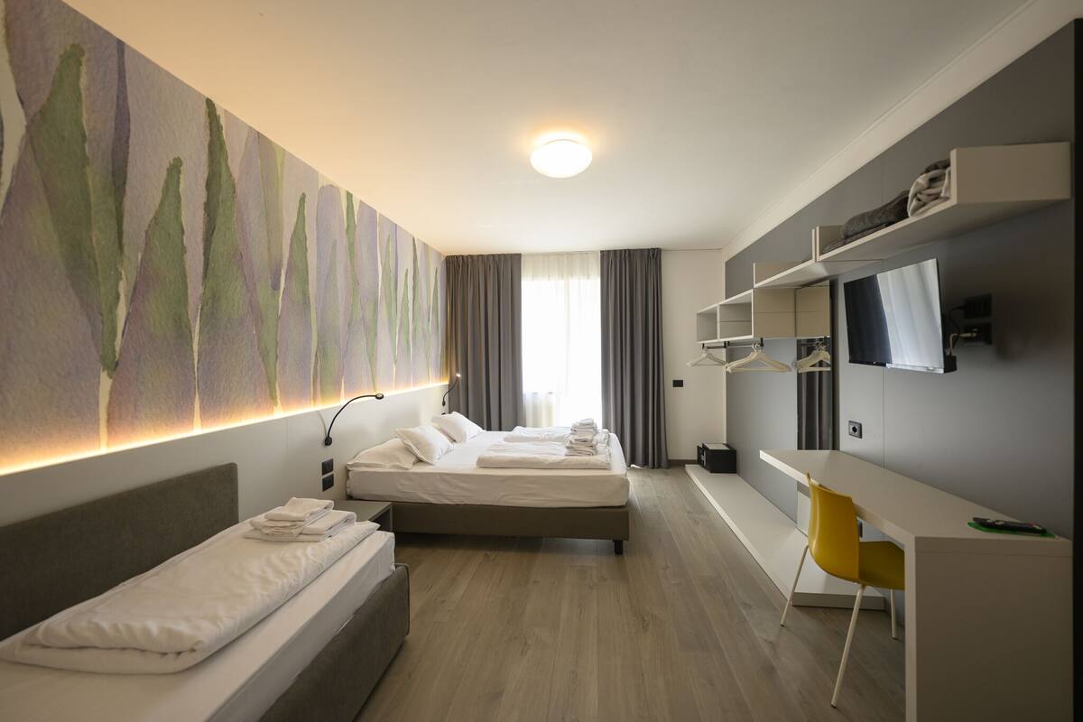 A modern hotel room with two beds, a desk, a chair, a TV, and a painting on the wall.
