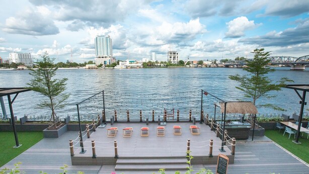 A waterfront deck with seating and a view of the city skyline. - The Royal River Hotel (Bangkok)