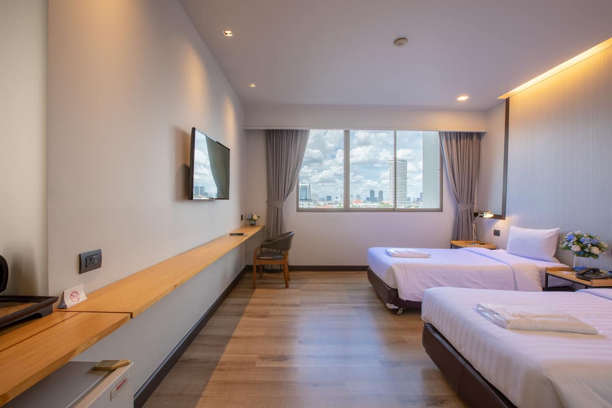 Hotellihuone, jossa on kaksi sänkyä, työpöytä, tuoli, seinälle asennettu televisio ja ikkuna, josta avautuu näkymä kaupunkiin.