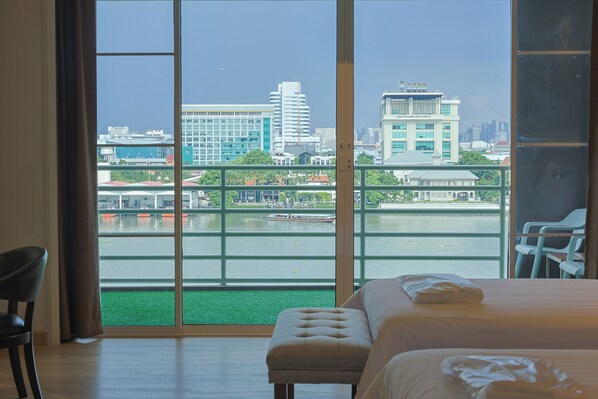 Habitación de hotel con un amplio ventanal corredera que da a un balcón con vistas a un río y edificios de la ciudad.