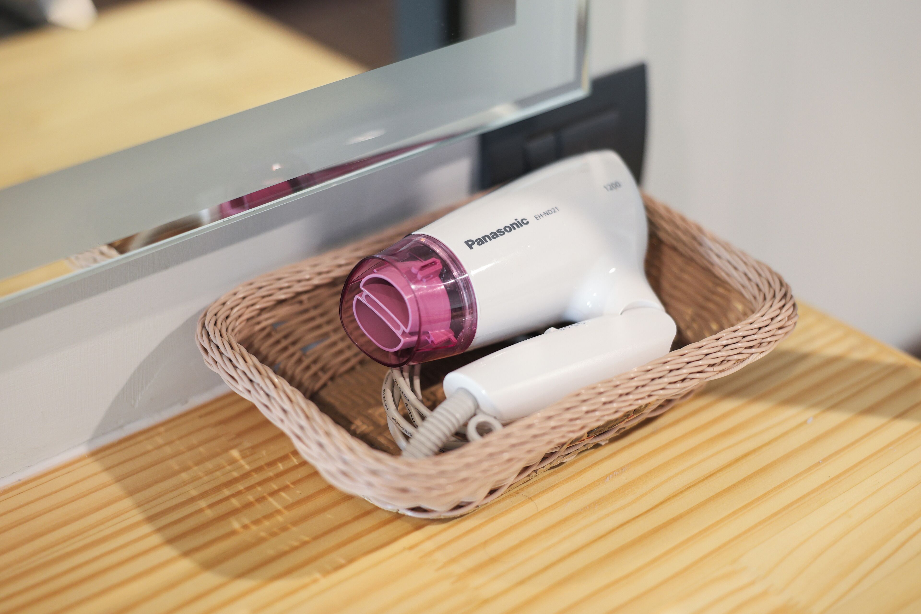 A Panasonic hairdryer in a woven basket on a wooden surface.