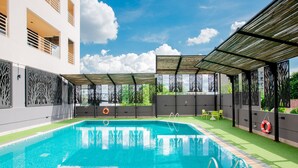 A swimming pool with a tiled deck, a covered seating area, and a view of a building in the background. - The Royal River Hotel (Bangkok)