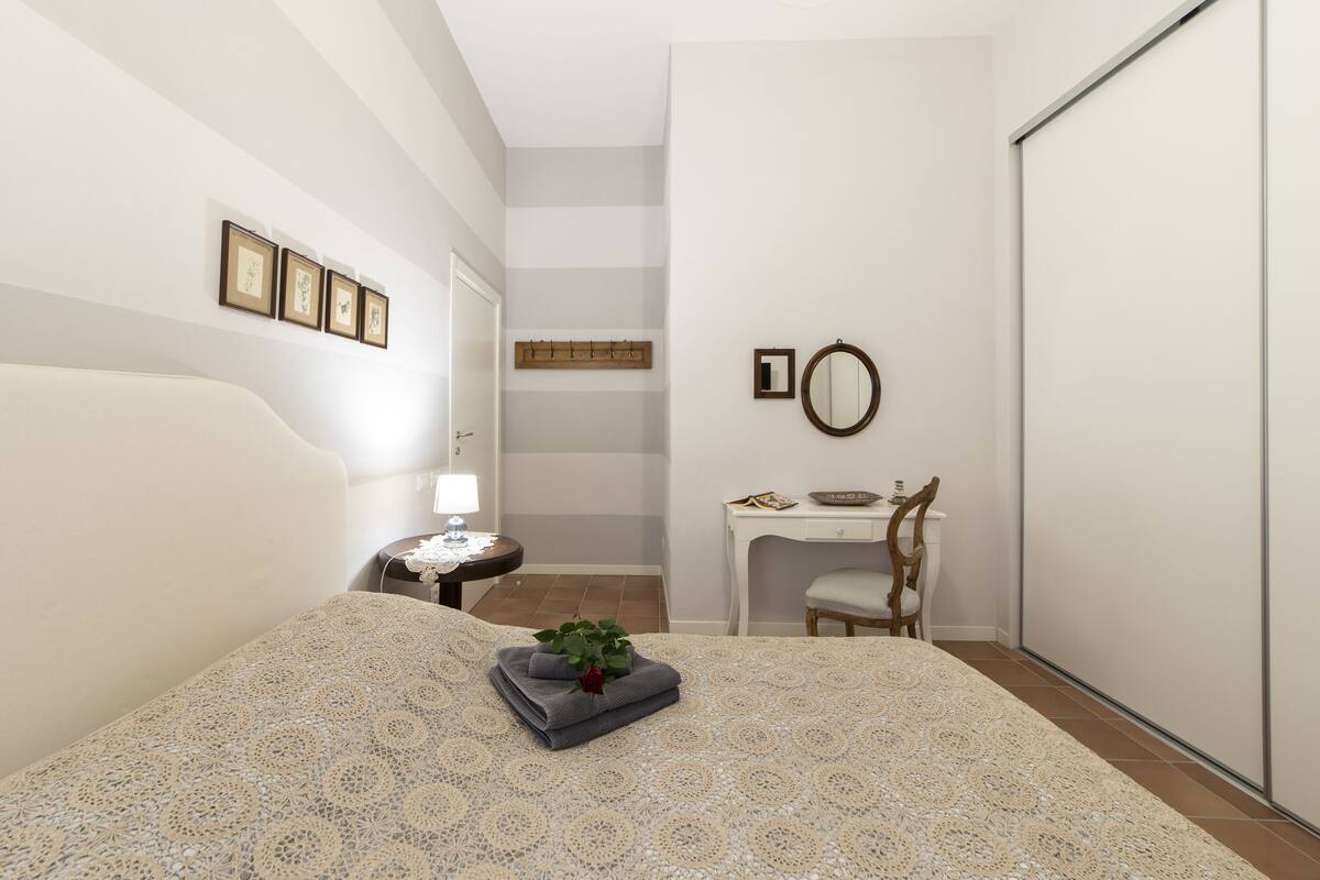 Ein Schlafzimmer mit Bett, Nachttisch, Lampe, Stuhl, Schreibtisch und Spiegel.
