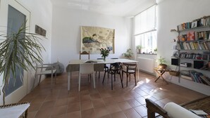A spacious living area with a dining table, chairs, a bookshelf, and a large window providing natural light. - Dogana d'Acqua Art B&B (Livorno)