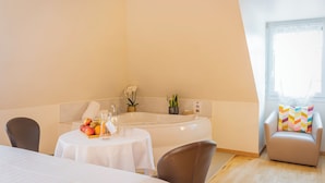 Una habitación con bañera, una mesa de comedor con fruta, una silla y un ventanal con cortinas.