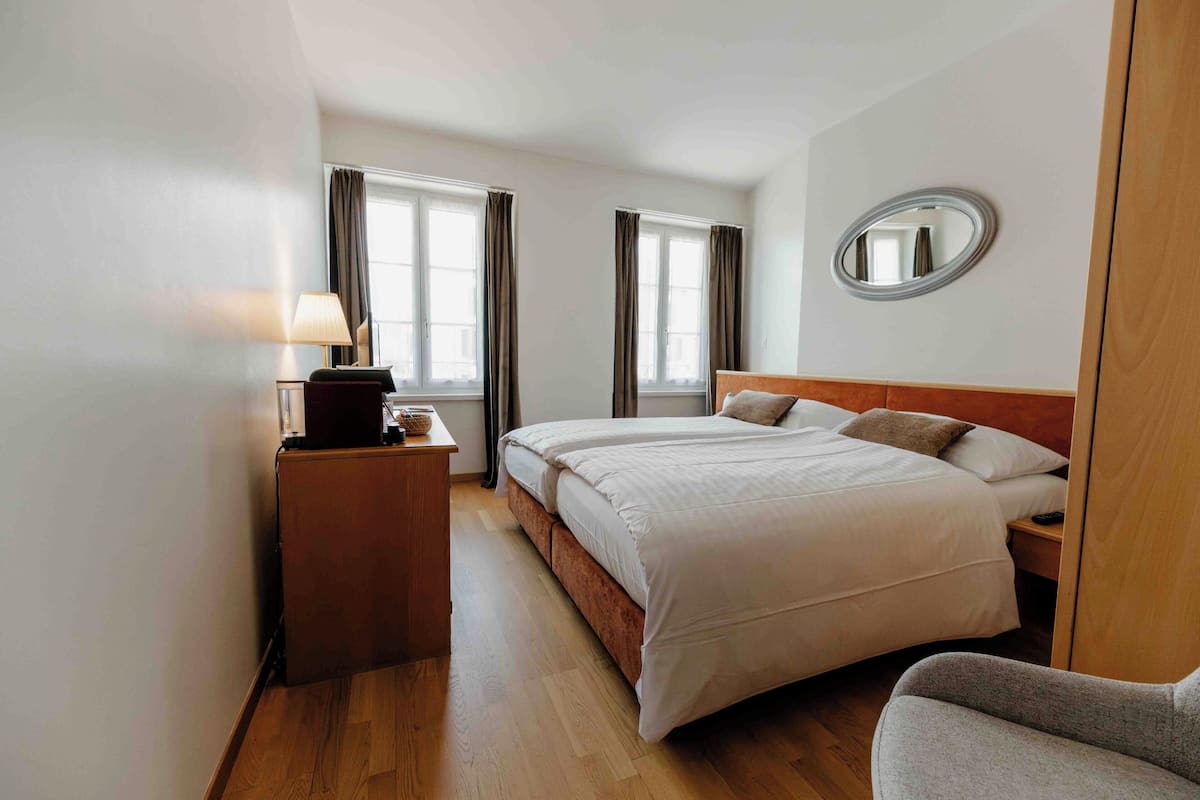 A hotel room with a bed, bedside table, lamp, and a mirror on the wall.