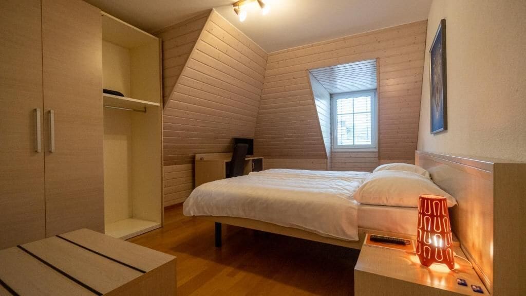 Een slaapkamer met een bed, een kledingkast, een bureau en een raam.