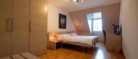 A bedroom with a bed, bedside table, lamp, and a television.