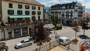 Un balcón con piso de madera, con vista a una calle con coches estacionados y un edificio con múltiples ventanas y balcones.
