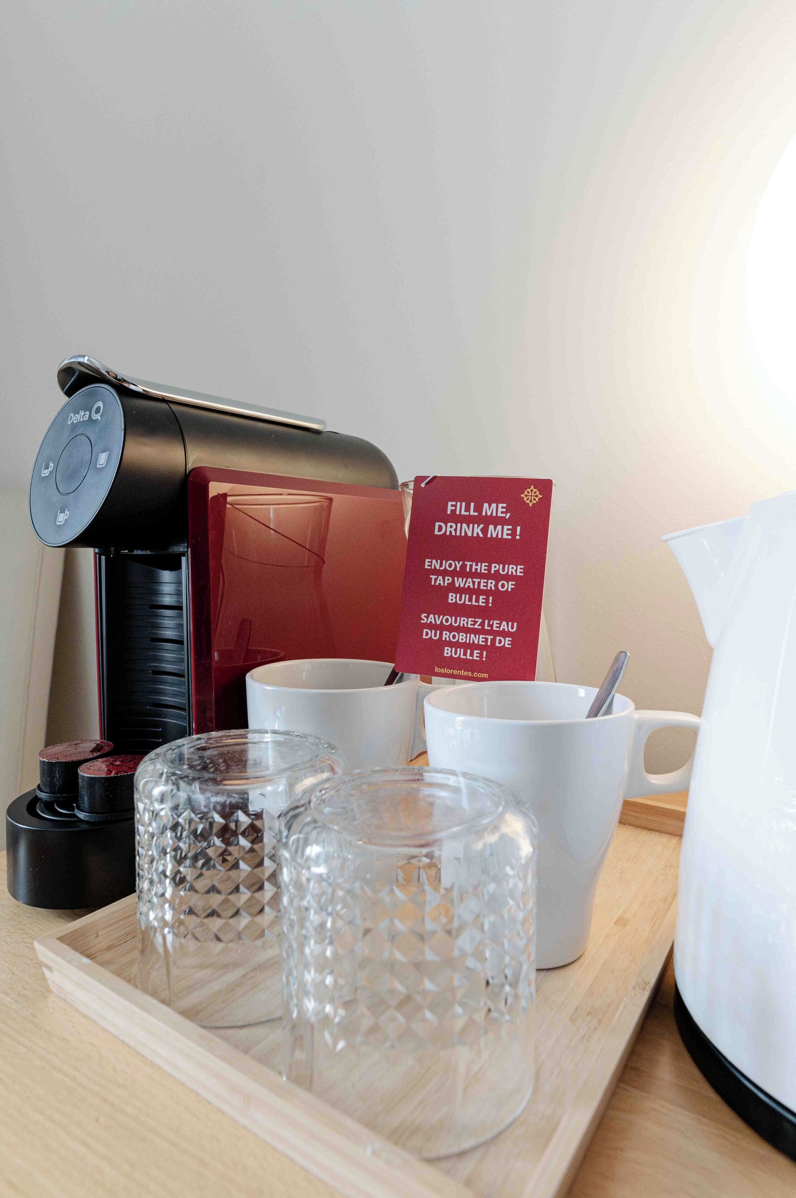 A coffee maker, a sign, cups, and a tray with glassware.