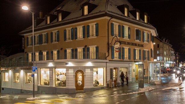 Un hotel de estilo arquitectónico europeo clásico, con una entrada destacada de fachada de vidrio y un letrero que indica que es el HOTEL DU CREVAL BLANC.