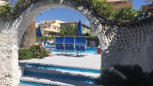 Zona de piscina con sillas azules y una piscina azul cristalina, enmarcada por muros de piedra blanca.
