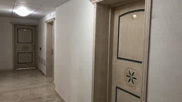 Un corridoio con una porta in legno, una targhetta numerica, un lampadario a soffitto e un pavimento tappezzato.