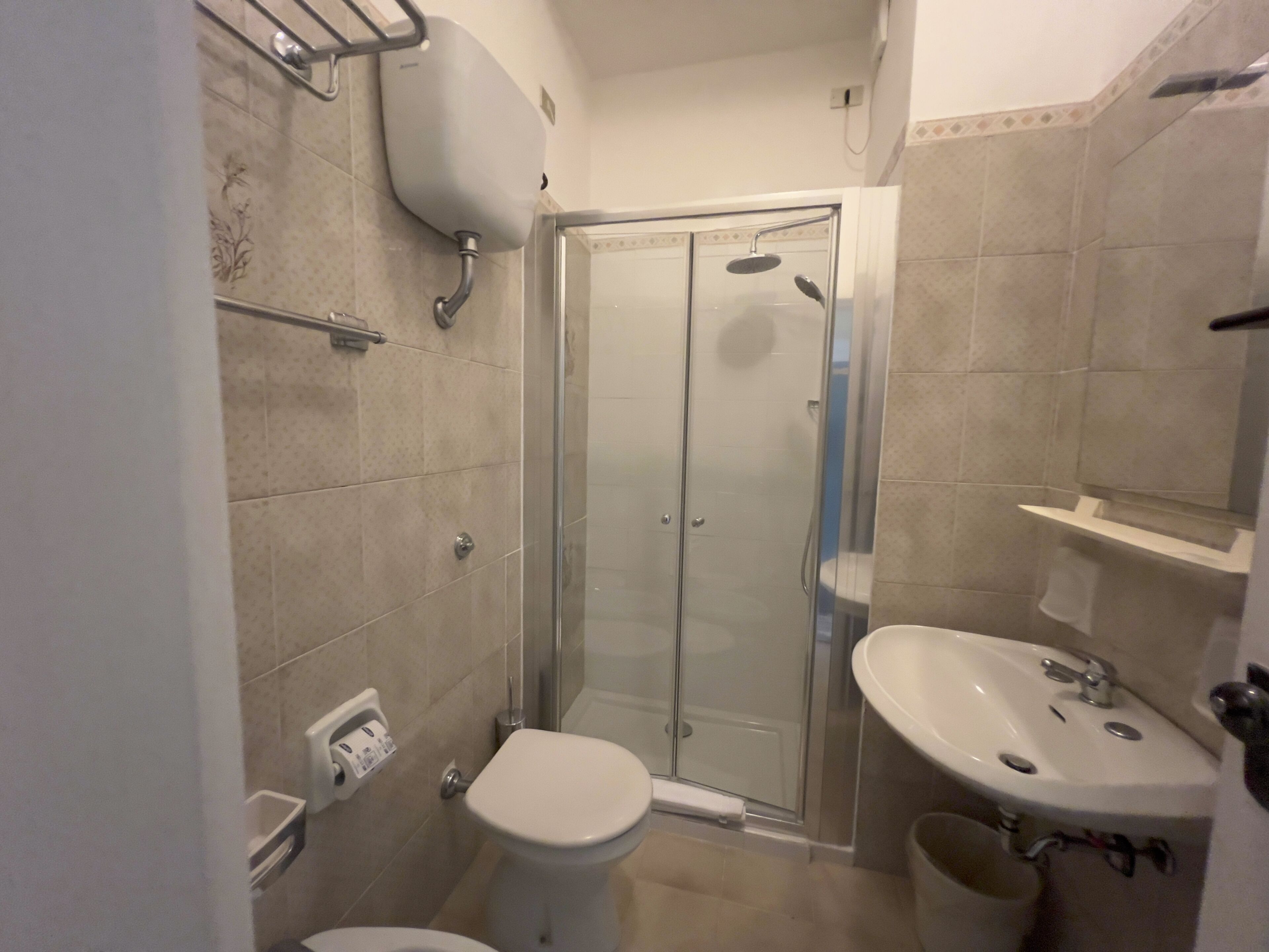 Un baño con inodoro, lavamanos, cabina de ducha y dispensador de papel higiénico.