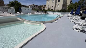 A swimming pool with a curved edge, surrounded by white lounge chairs and blue umbrellas.