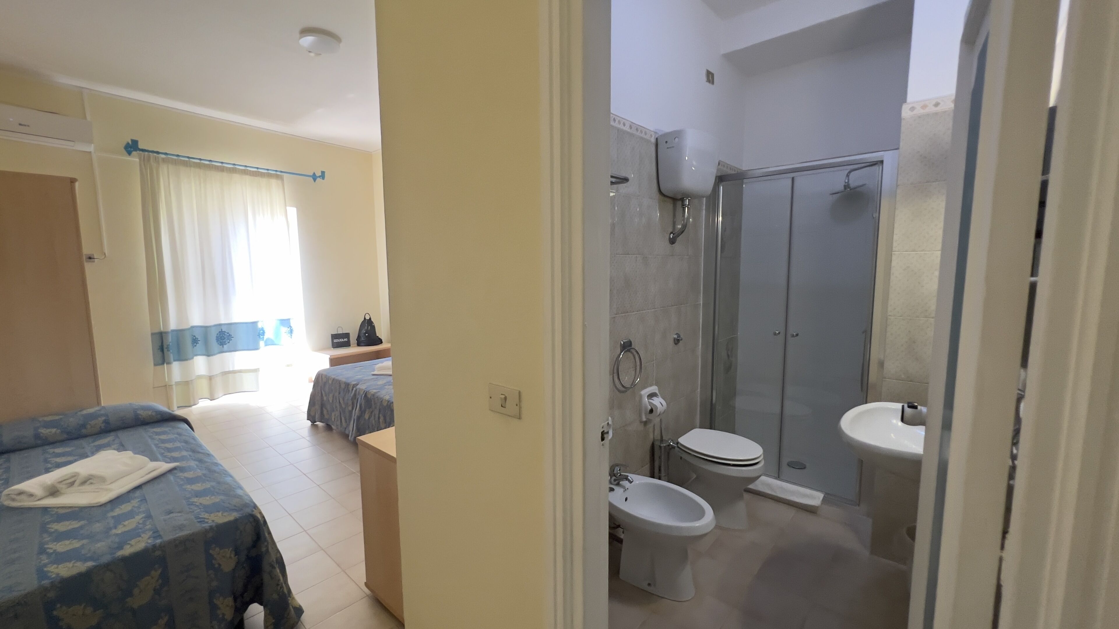 Ein Hotelzimmer mit Bett, Nachttisch, Bad mit Dusche, Toilette und Waschbecken.