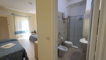 Una habitación de hotel con cama, mesita de noche, baño con ducha, inodoro y lavabo.