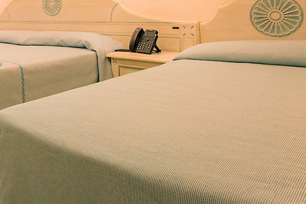 A hotel room with two single beds, a bedside phone, and a curtain with a blue pattern.