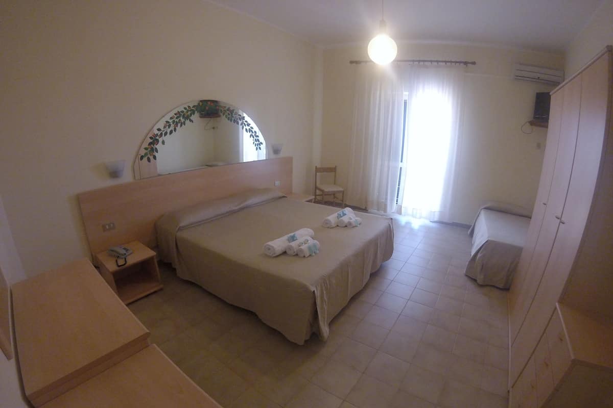 A hotel room with a single bed, a bedside table with a phone, a chair, and a wardrobe.