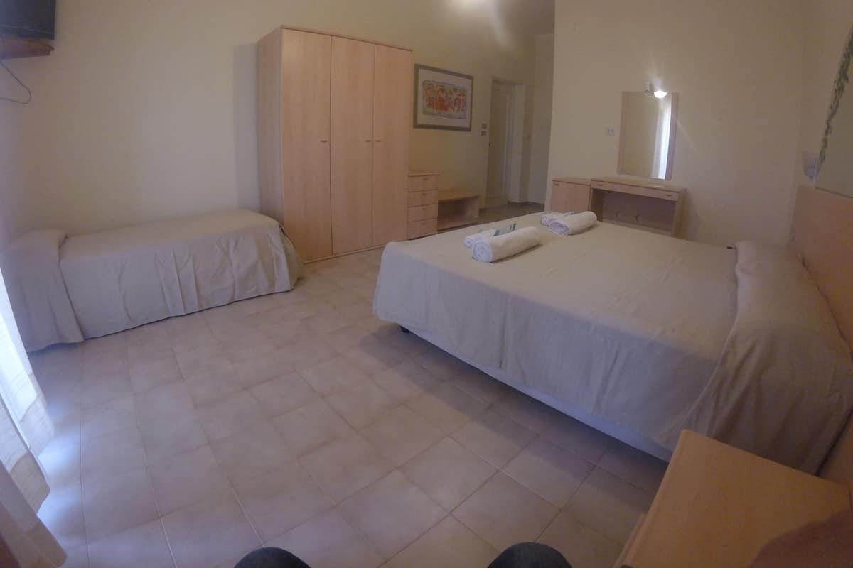 A room with a bed, a bench, a wardrobe, and a desk with a mirror.