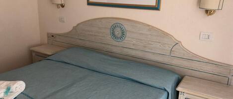 A bedroom with a bed, a nightstand, a wall-mounted lamp, and a painting.