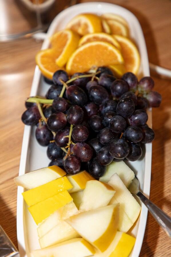 A white rectangular plate with sliced oranges, grapes, and apple wedges.