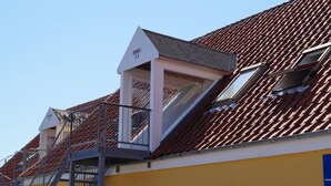 Un bâtiment avec un toit recouvert de tuiles rouges, un mur jaune et un escalier menant à un étage supérieur.