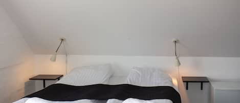 Un lit jumeau bien fait, avec du linge de lit blanc et un plaid noir, deux tables de chevet avec des lampes et un plafond blanc.