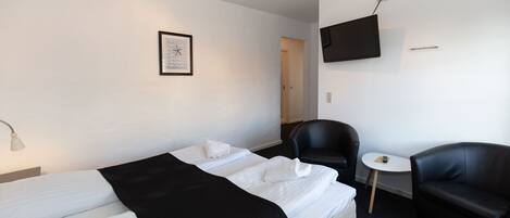 Habitación de hotel con dos camas, un escritorio, una silla, un televisor y una mesita.