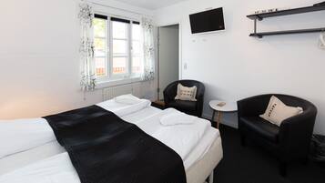 Habitación de hotel con cama, dos sillas, una mesita y televisor en la pared.