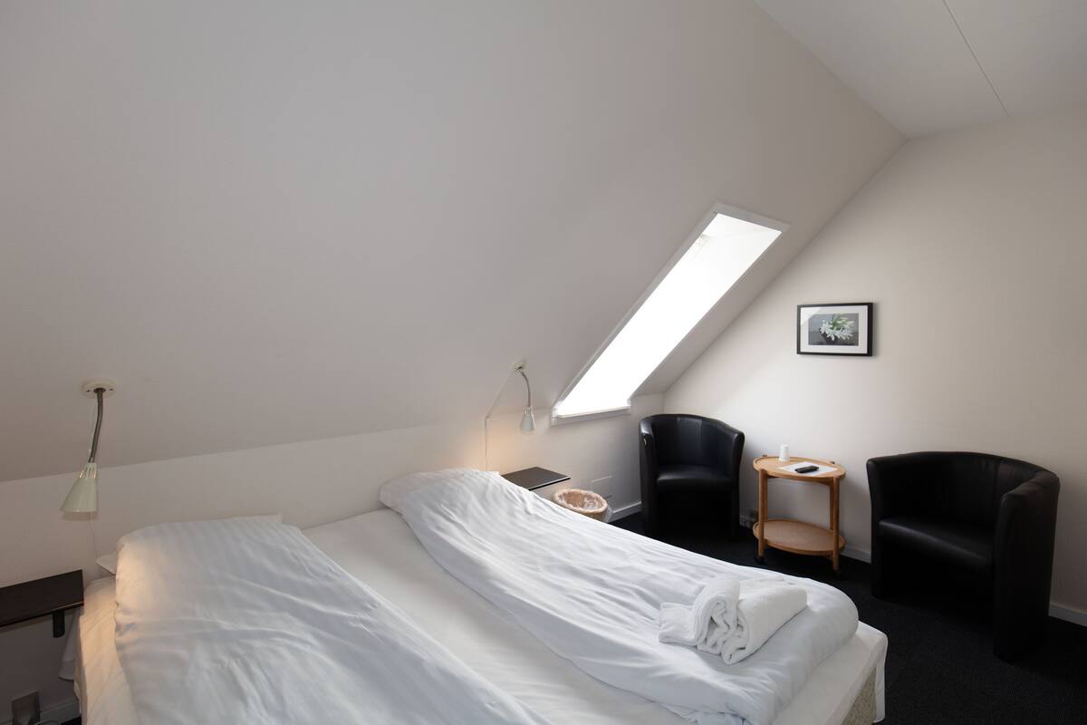 Un dormitorio con cama, escritorio, silla, mesita y tragaluz.