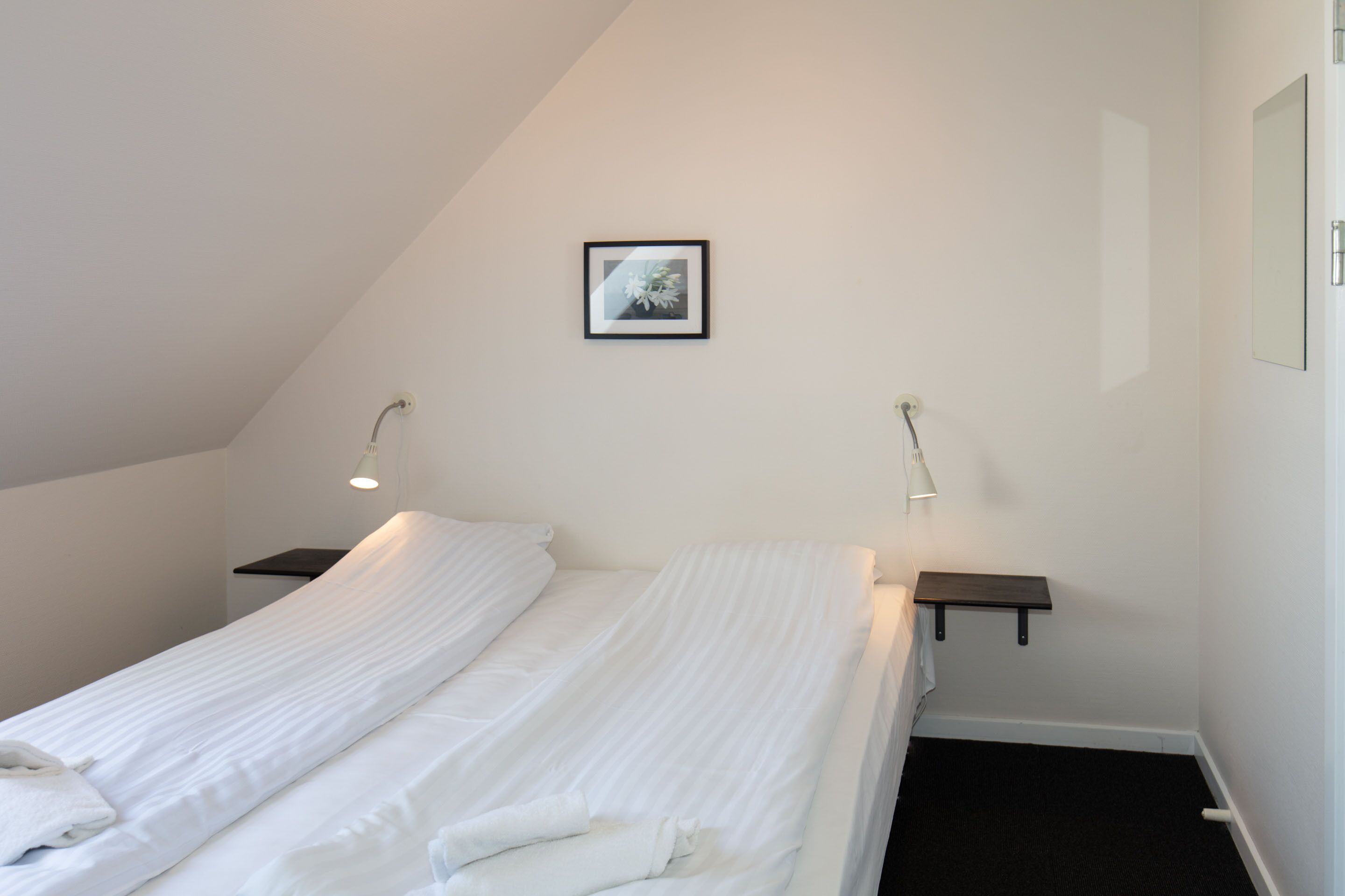 A bedroom with a single bed, two bedside tables, a framed picture on the wall, and a small shelf.