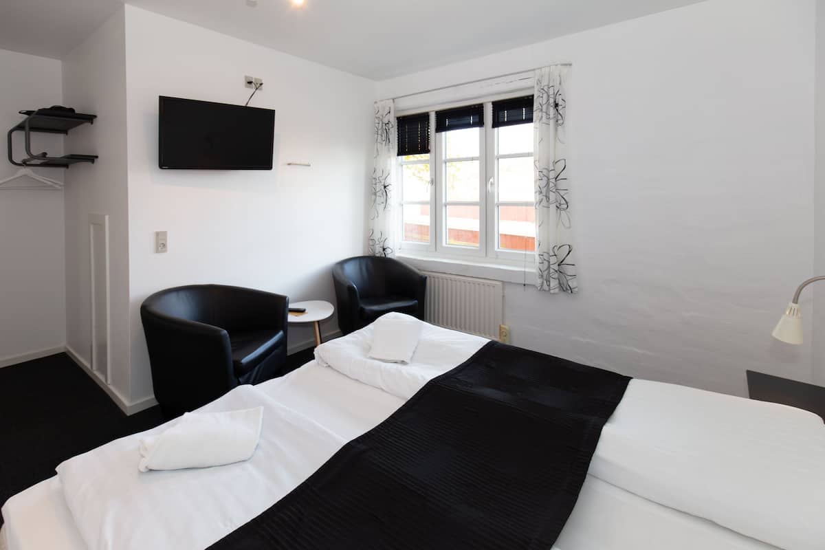 Habitación de hotel con cama, dos sillas, una mesita, televisor y ventana con cortinas.