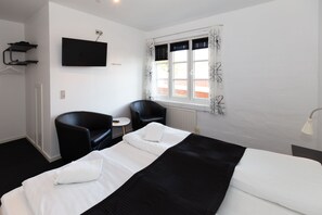 A hotel room with a bed, two chairs, a small table, a TV, and a window with curtains.