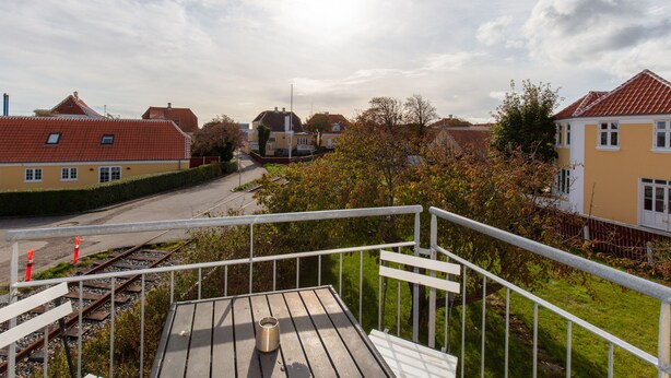 Un balcon doté d’une rambarde en métal, donnant sur une voie ferrée et les maisons voisines.