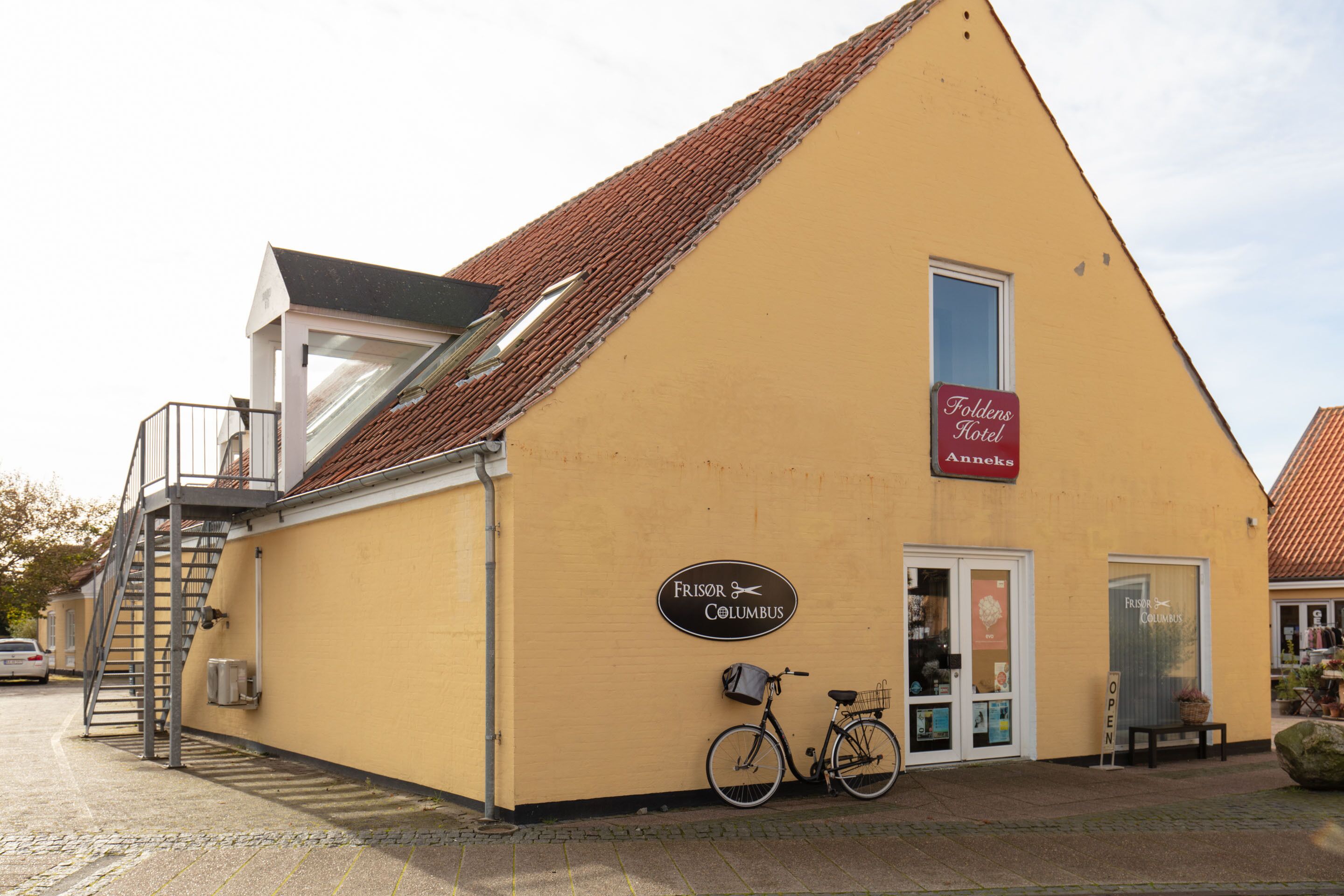 A yellow building with a sign for Frisor Columbus, a staircase, and a bicycle parked outside.