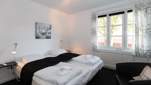 Une chambre d’hôtel avec un grand lit, une table de chevet avec une lampe, une chaise et une fenêtre avec des rideaux.
