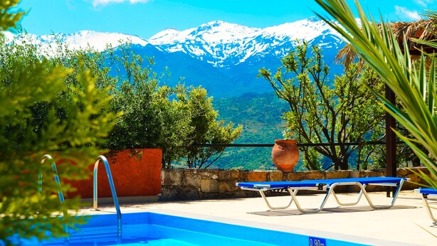 Ein Pool mit Blick auf die Berge, eine Steinmauer und ein blauer Liegestuhl.
