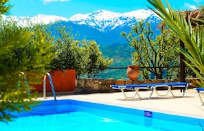 A pool with a mountain view, a stone wall, and a blue lounge chair.