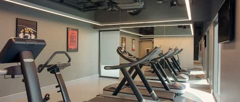 Un gimnasio con cintas de correr y elípticas, un espejo grande y carteles motivacionales.