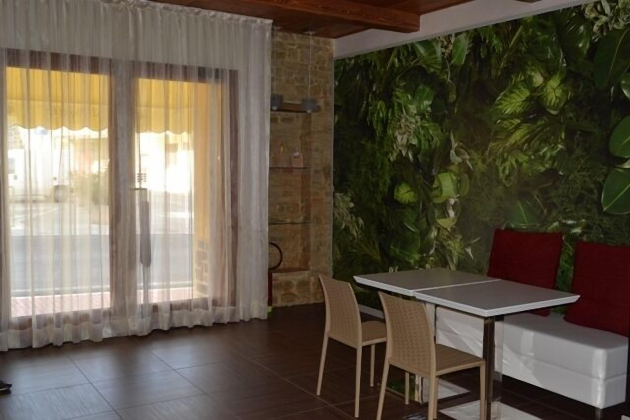 A room with a dining table, chairs, a sofa, and a large window with sheer curtains.