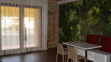 A room with a dining table, chairs, a sofa, and a large window with sheer curtains.