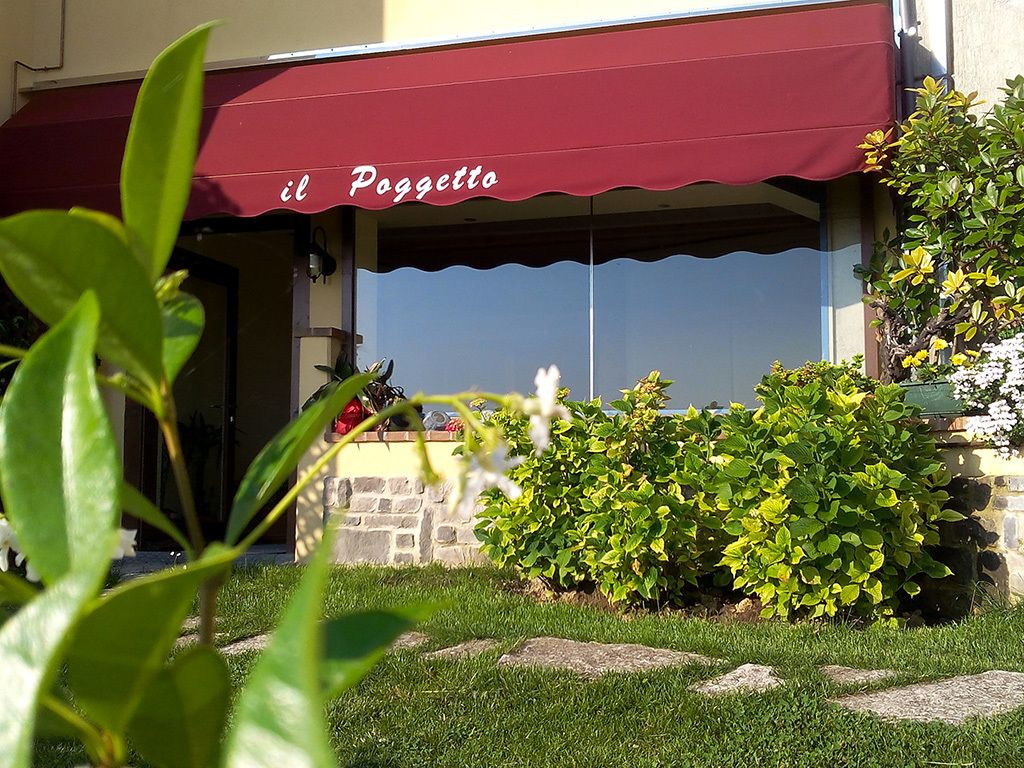 A restaurant named "il Poggetto" with a red awning, stone wall, and green plants in the foreground.